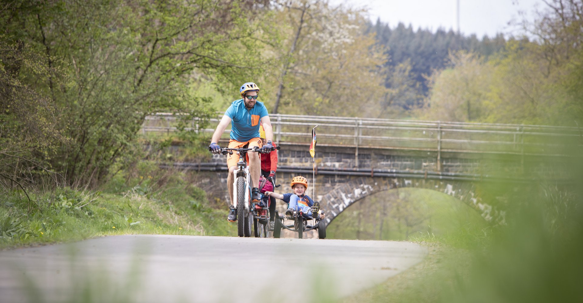 Ein Mann fährt auf dem Bahnradweg Fahrrad und hat zwei Kinder in Kinderanhängern dabei