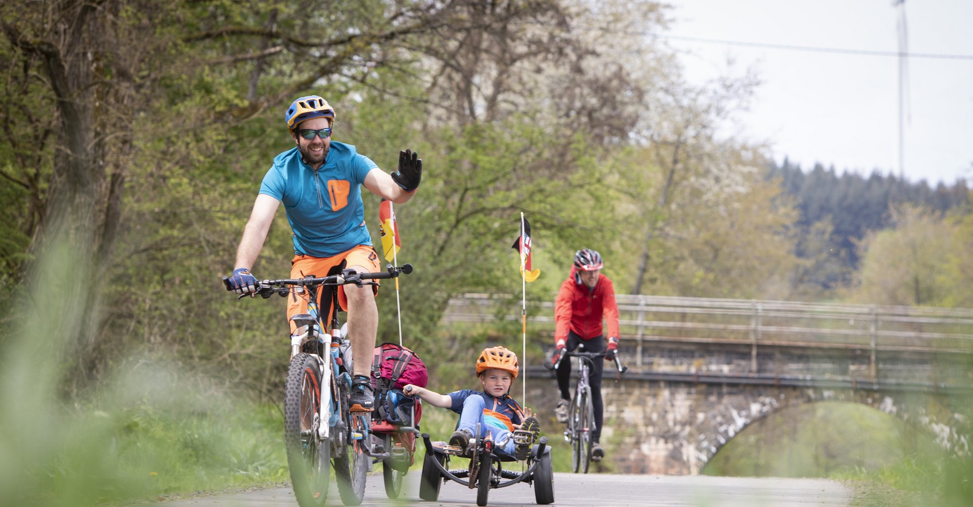 Ein Mann fährt auf dem Bahnradweg Fahrrad und hat zwei Kinder in Kinderanhängern dabei. Im Hintergrund erkennt man einen weiteren Radfahrer
