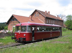 Einfahrt der Hochwaldbahn in den Bahnhof Nonnweiler. Der Museumszug steht auf den Gleisen vor dem Bahnhofsgebäude des Bahnhofs Nonnweiler. Im Vordergrund des Bildes ist grüne Wiese zu sehen
