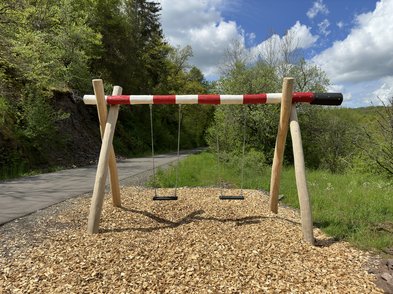 eine Schaukel aus Holz steht am Rande des Bahnradwegs