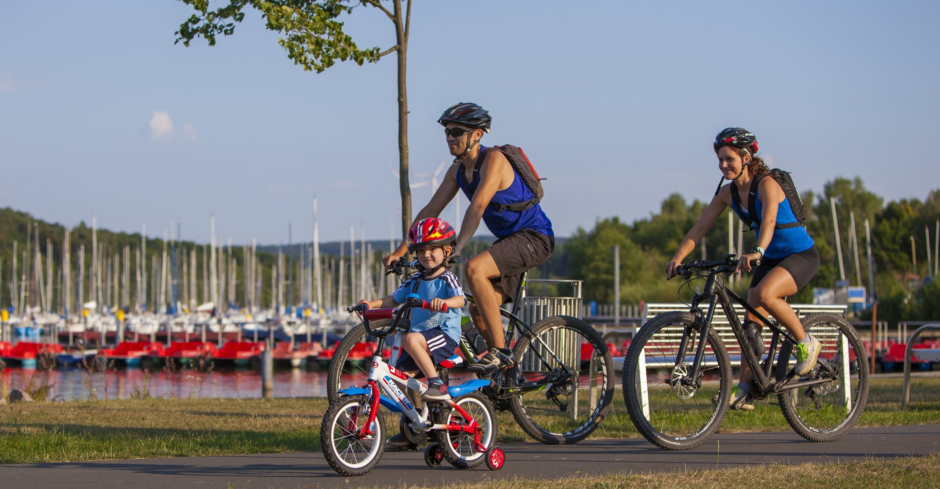 Eine Familie (Mann Frau und Kind) führt am Rande des Bostalsees Fahrrad