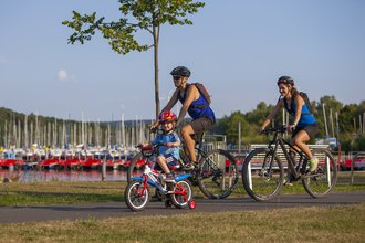 Eine Familie (Mann Frau und Kind) führt am Rande des Bostalsees Fahrrad