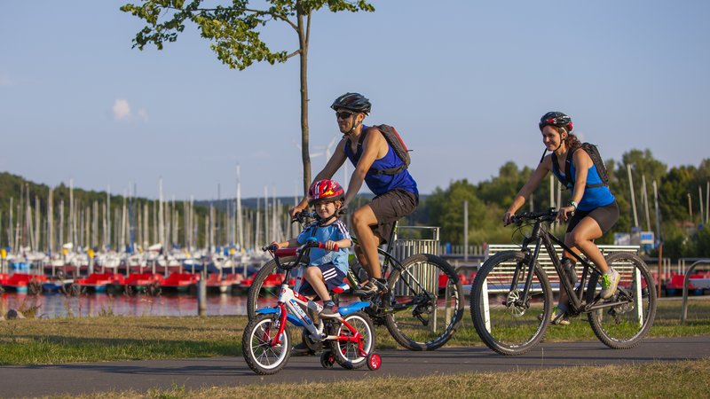 Eine Familie (Mann Frau und Kind) führt am Rande des Bostalsees Fahrrad