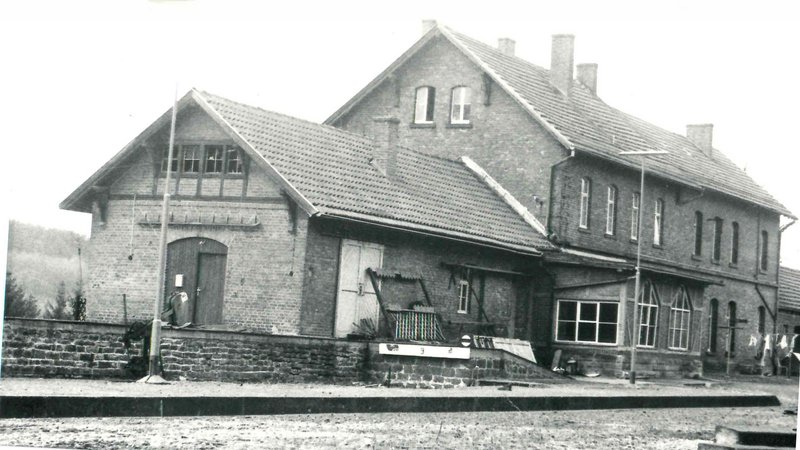 © Bernd Melcher, Sammlung Georg Dollwet schwarz-weiß Aufnahme des Bahnhofgebäudes in Nonnweiler aus dem Jahr 1978. Es besteht aus 2 aneinander gebauten Häuschen, das linke ist etwas kleiner und niedriger, der rechte etwas höher und größer.