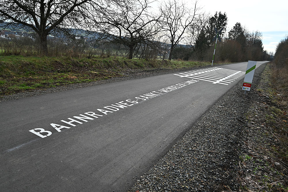 Gleismarkierungen sowie Schriftzug der Website Bahnradweg Sankt Wendeler Land auf dem asphaltierten Radweg